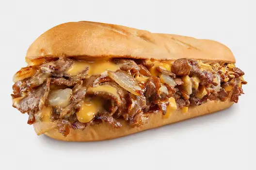 Chicken Philly Cheesesteak from Charleys Nottingham Cheesesteaks against a white background. This is make with grilled chicken, peppers, and onions with provolone on a toasted roll. This is served with lettuce, tomato, mayo, and pickle. Philly chicken cheesesteak near me.
